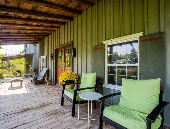 Industrial-style covered porch with corrugated metal walls, wooden beams, black chairs with green cushions, and views of surrounding landscape.